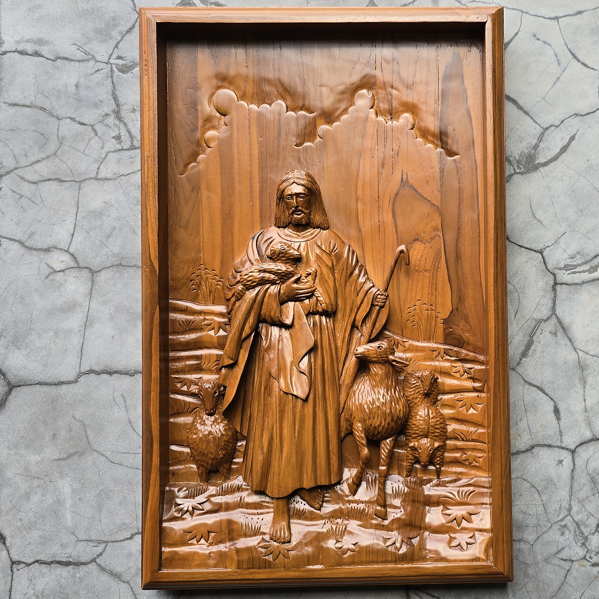 Wooden relief sculpture of a shepherd with two sheep against a textured gray wall.