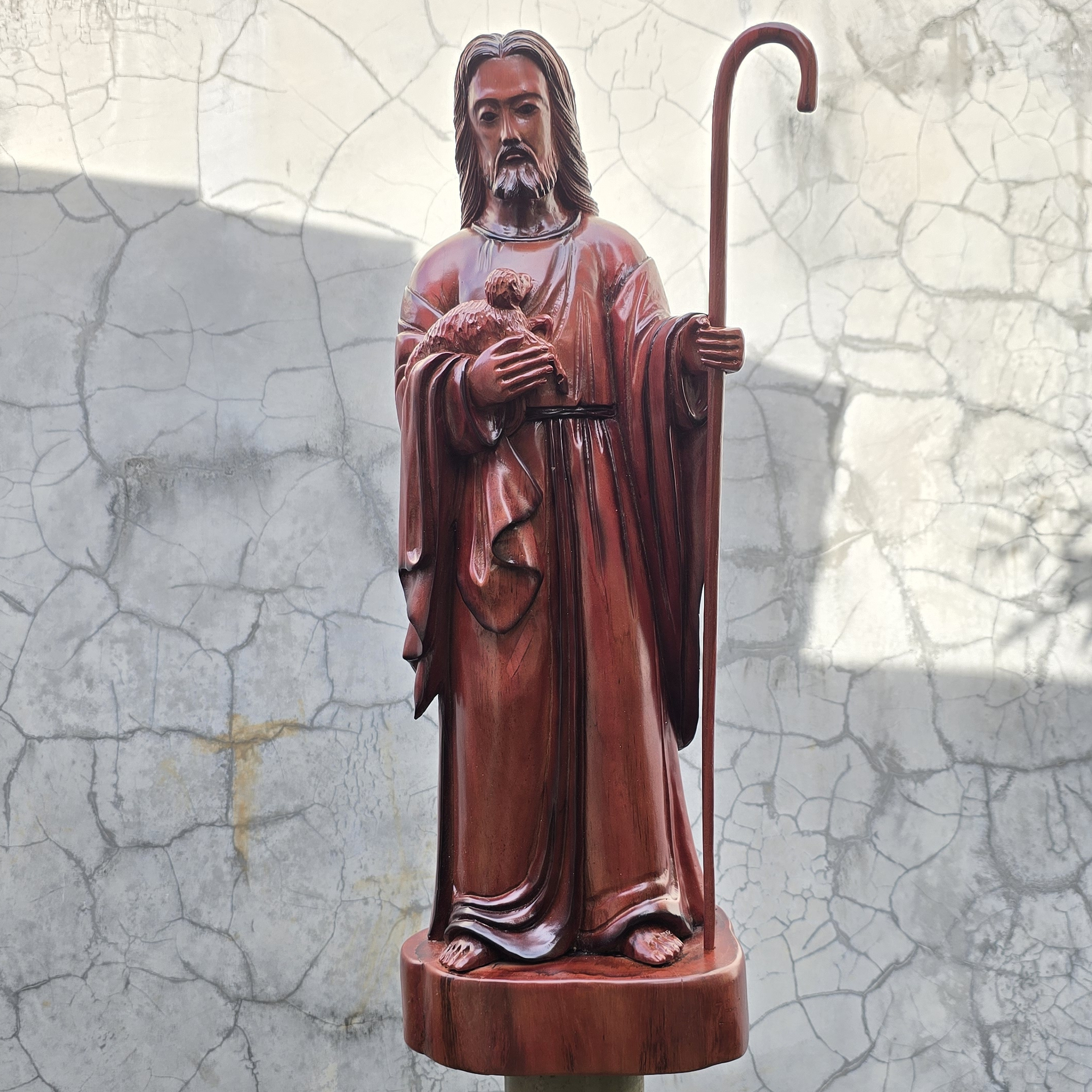 Statue of Jesus the shepherd holding a staff against a textured wall background