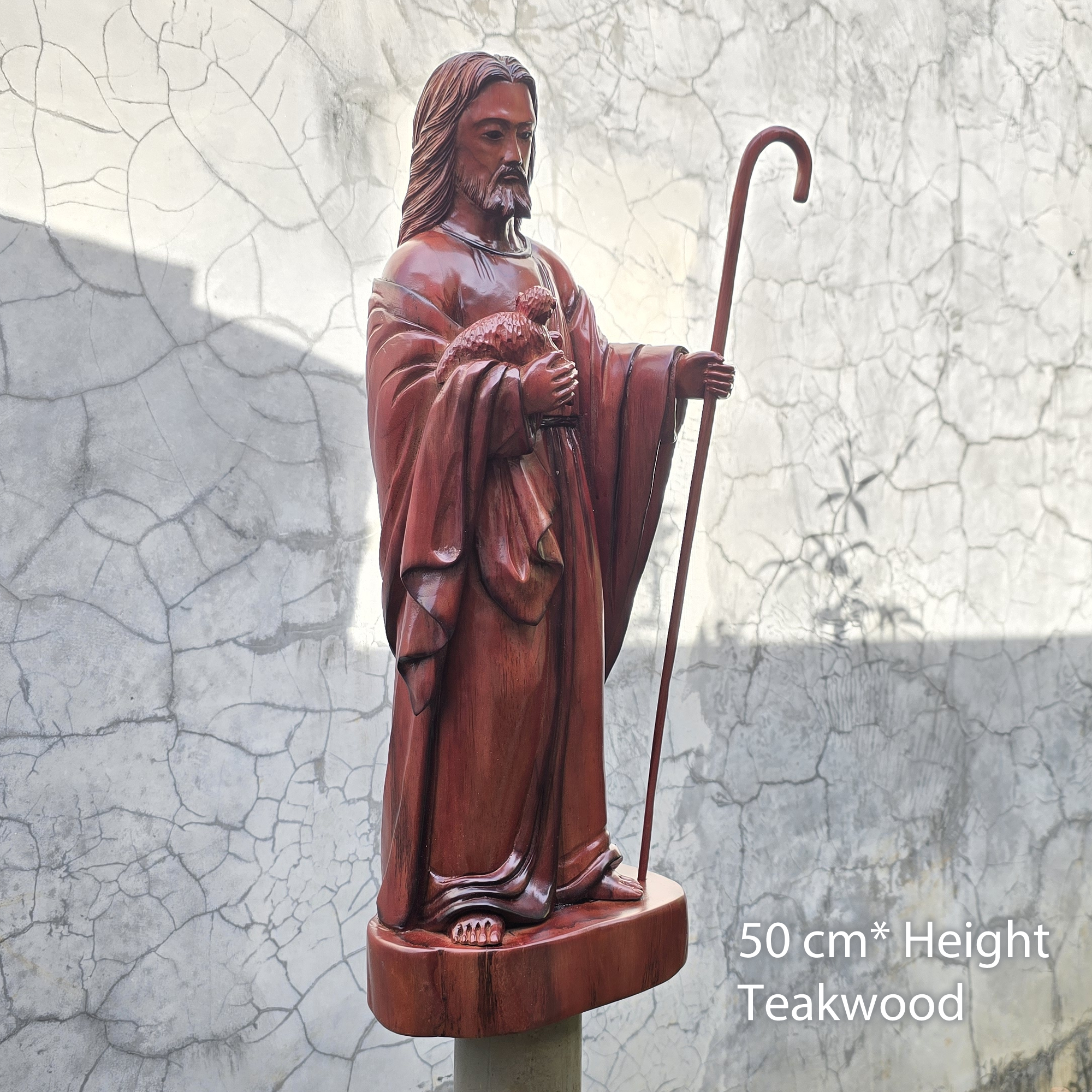 Wooden statue of a shepherd with a staff against a textured wall.