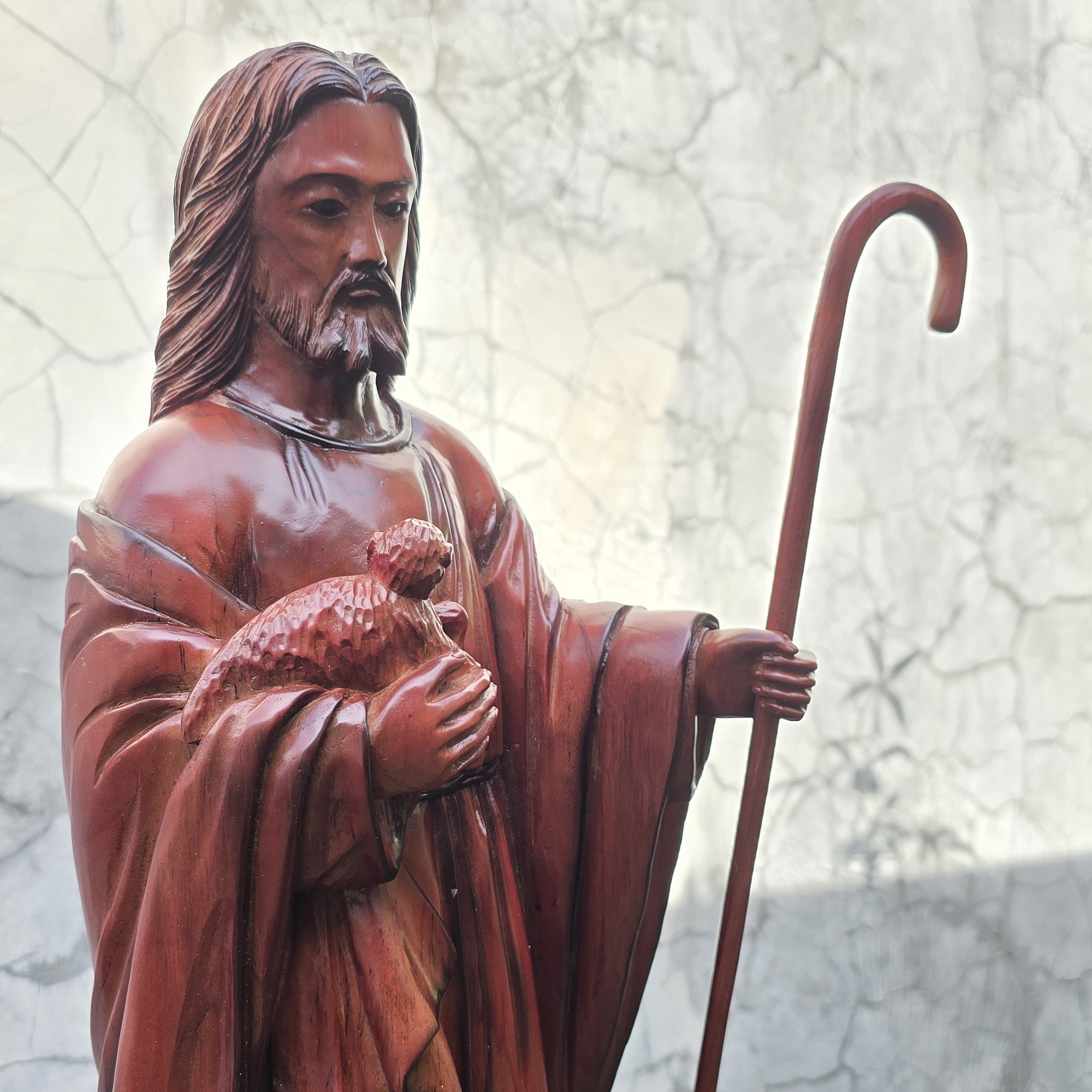 Statue of Jesus the shepherd holding a sheep and a staff against a textured white background