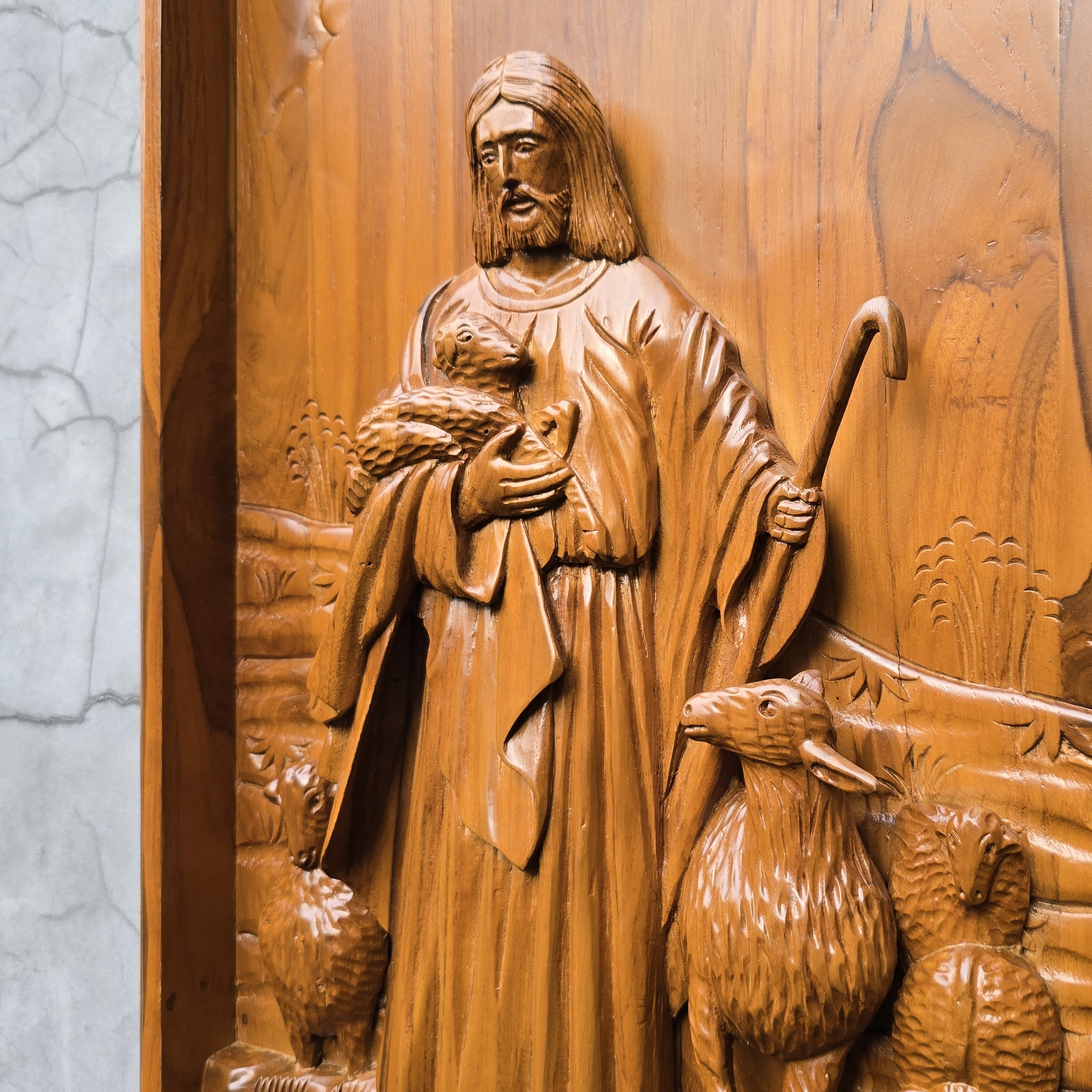 Wooden relief of a shepherd with a lamb on a textured wall.