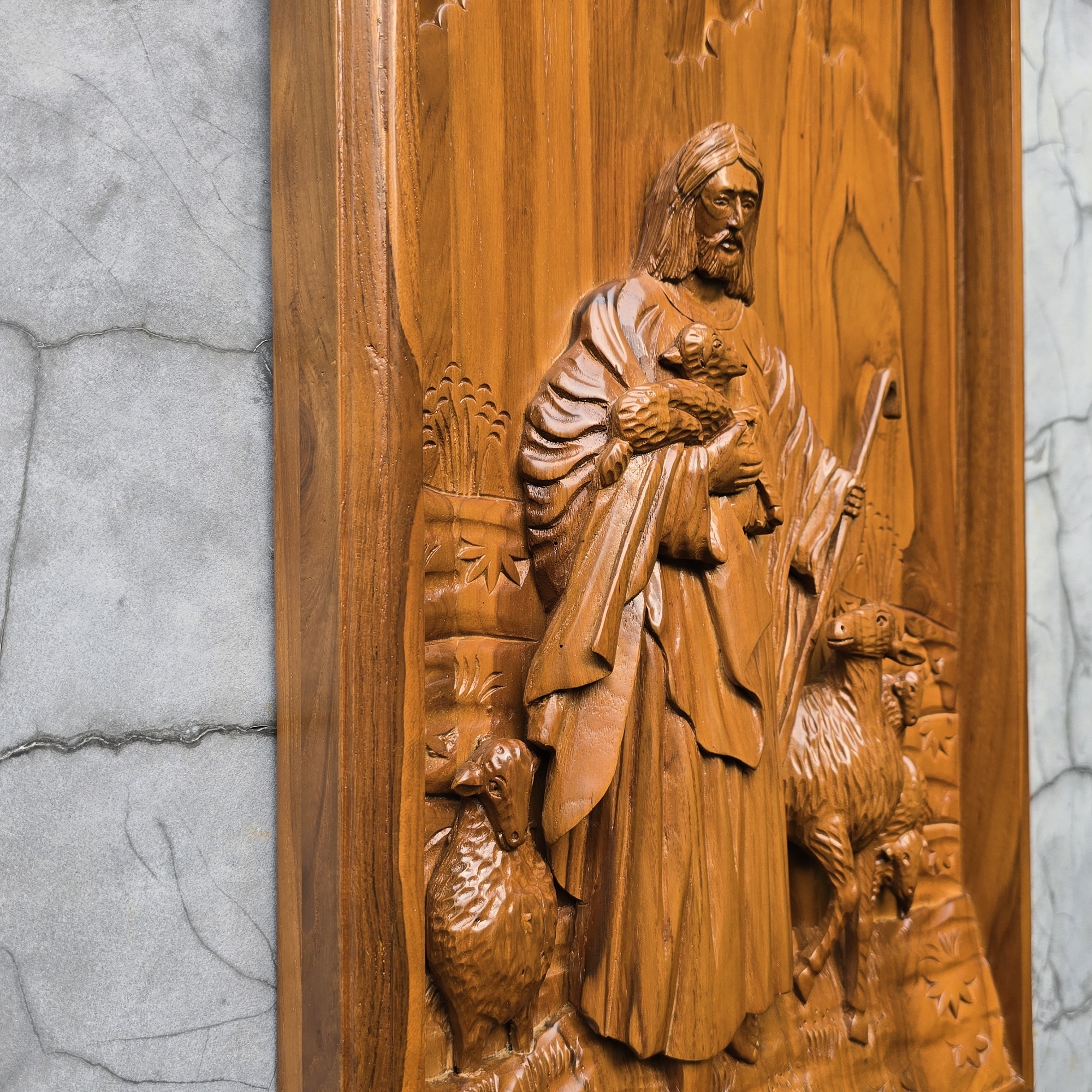 Wooden relief sculpture of a shepherd with sheep on a textured gray background