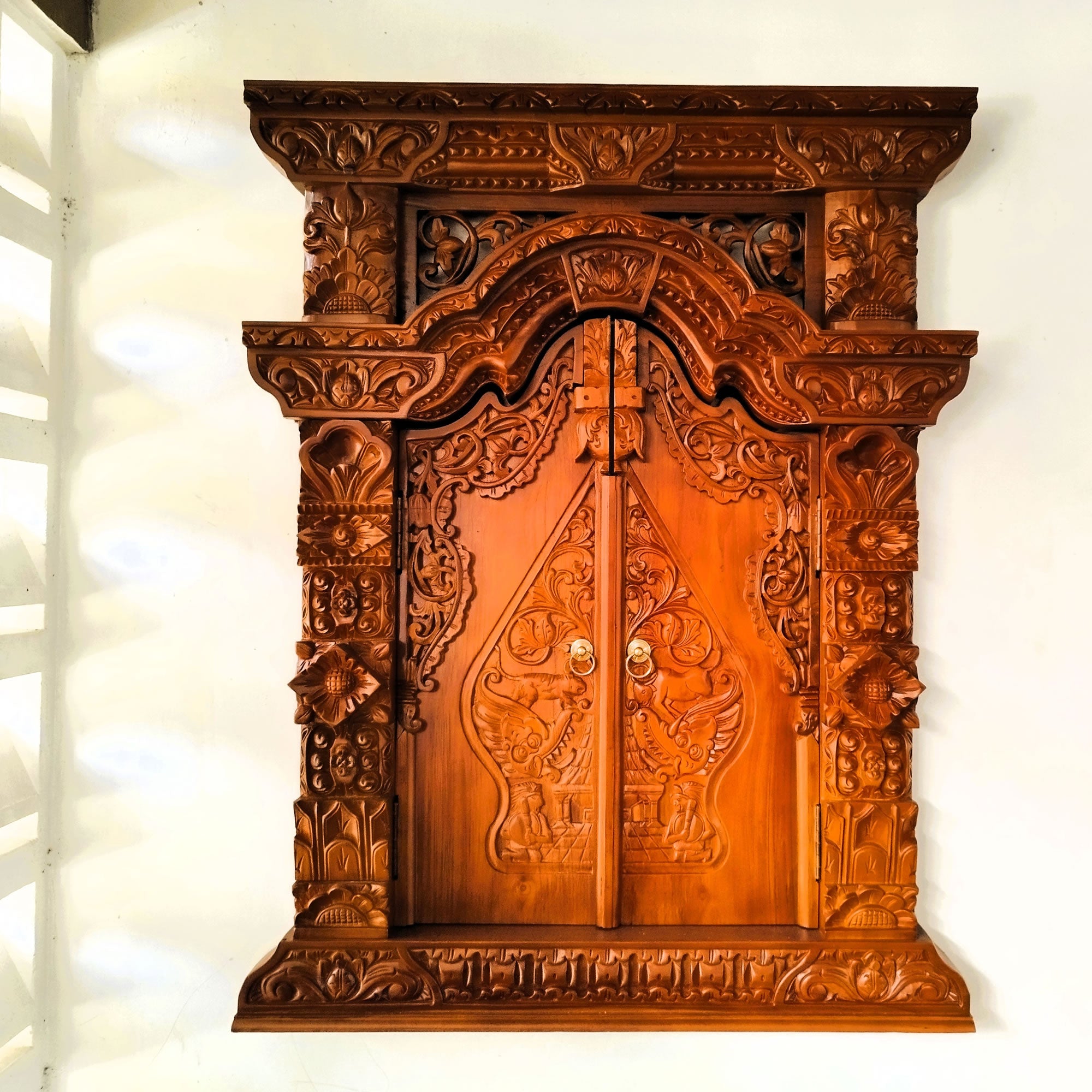 Frontal view of a hand-carved solid teakwood Gebyok wall art with doors closed, showing intricate Javanese floral carvings.
