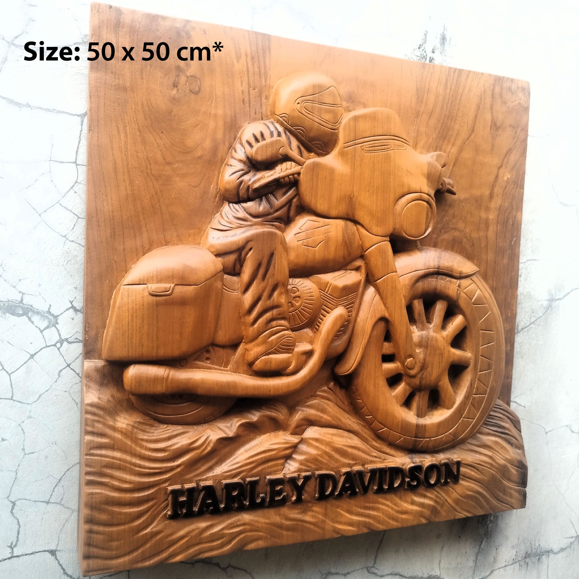 A rectangular wooden wall plaque featuring a carved Harley-Davidson motorcycle and rider, mounted against a light textured wall. The plaque has a size overlay reading 'Size: 50 x 50 cm*' in the top-left corner and the words 'HARLEY DAVIDSON' carved into the bottom edge.