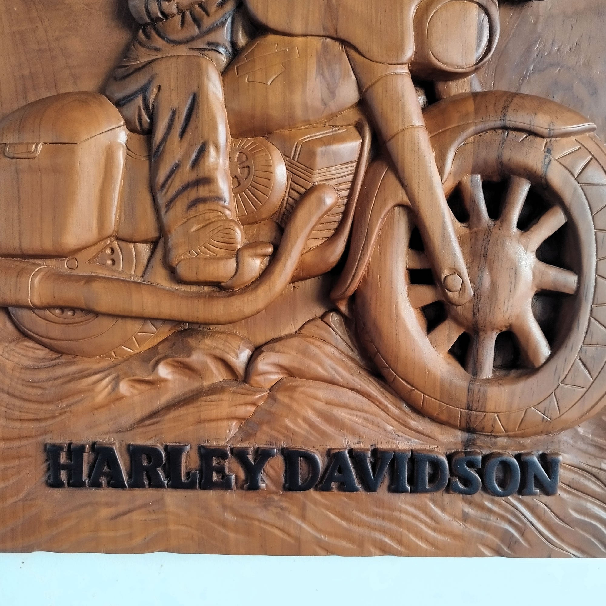 A carved wooden wall plaque featuring a motorcycle and rider in relief, with the words HARLEY DAVIDSON in raised letters at the bottom, photographed against a plain light background.