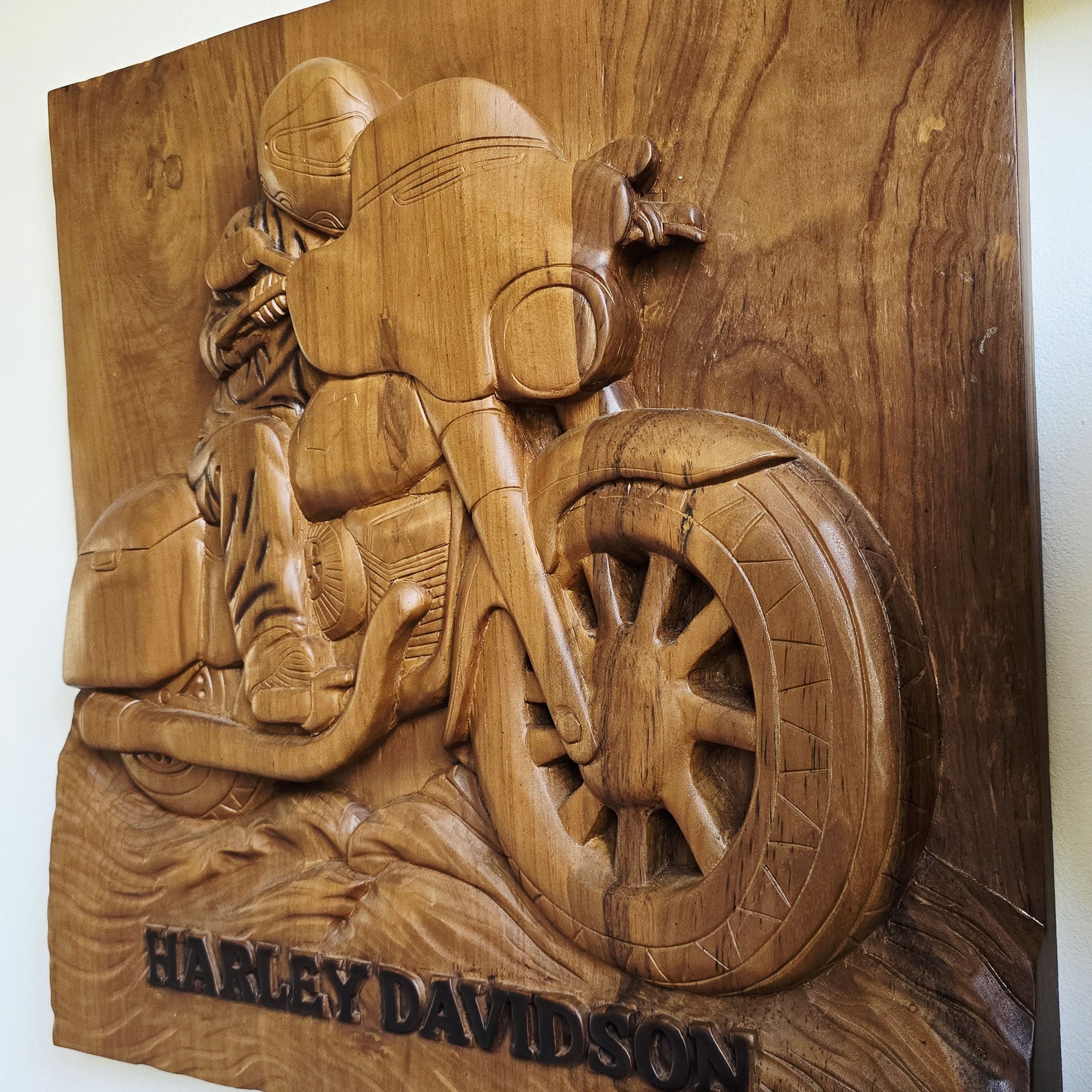 A hand-carved wooden wall plaque featuring a detailed relief of a Harley-Davidson motorcycle and rider, with the text 'HARLEY DAVIDSON' carved at the bottom, shown against a plain light background.