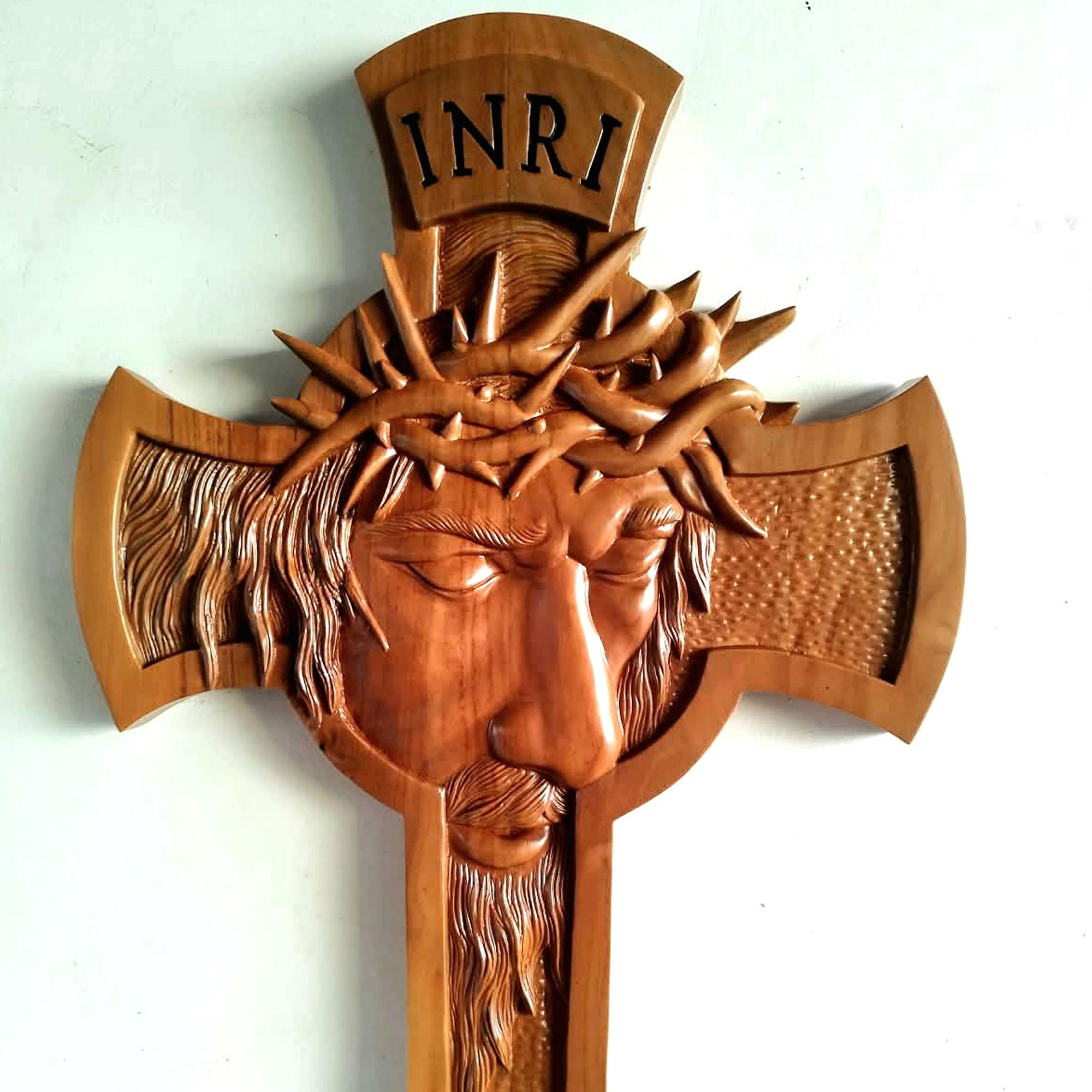 A hand-carved wooden Jesus Christ cross featuring a detailed face with a crown of thorns and the inscription 'INRI' at the top, shown against a plain light background.