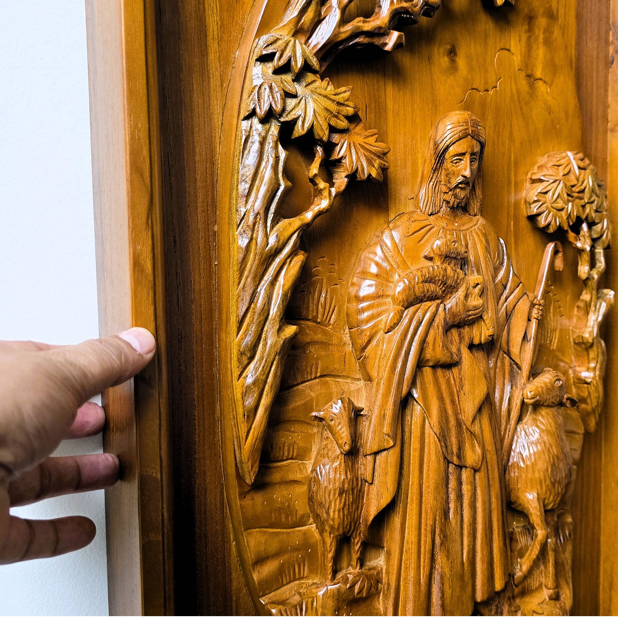 Detailed closeup of solid teak wood carving showing dimensional relief details of Jesus Christ as the sacred shepherd, hand-crafted wall sculpture.