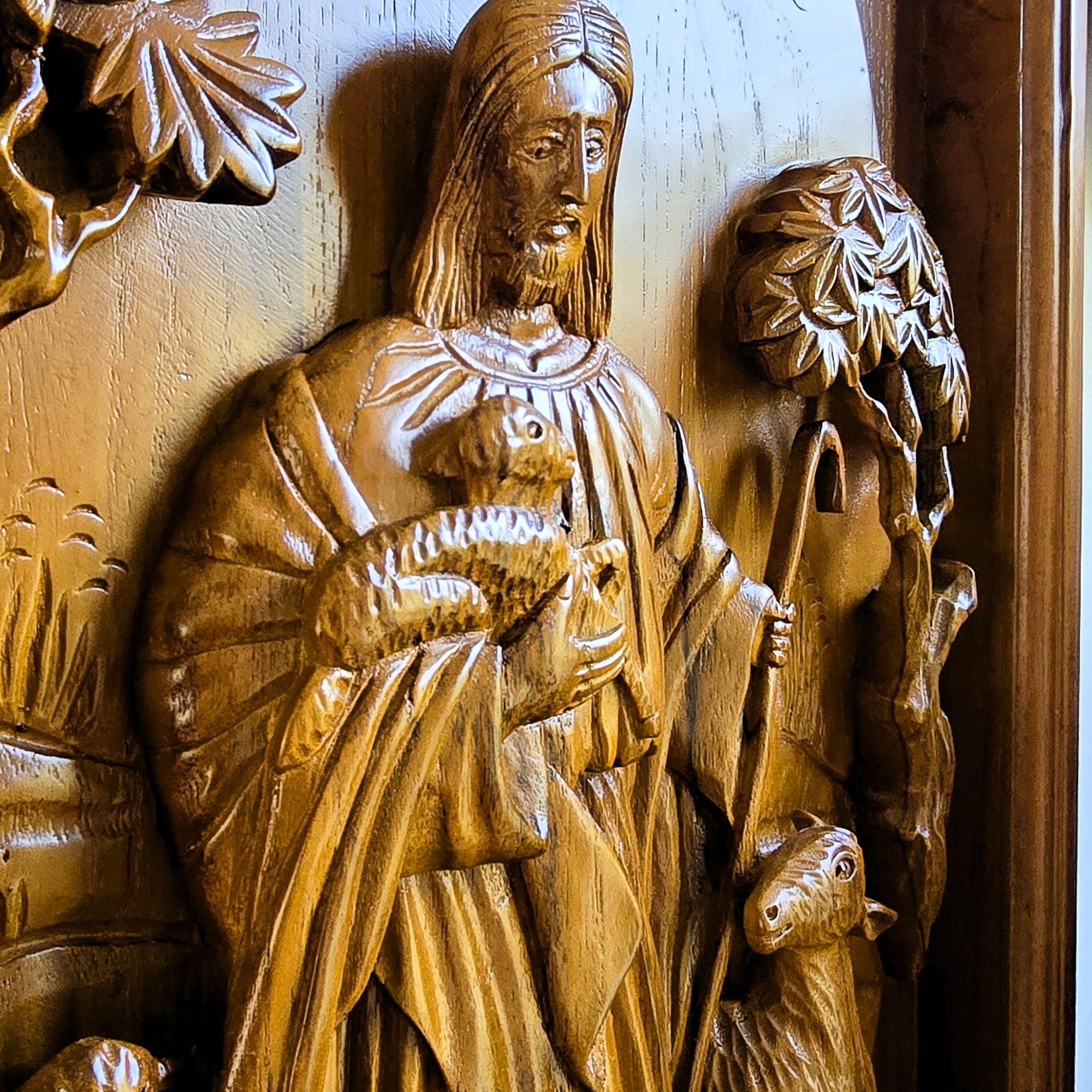 Detailed closeup of solid teak wood carving showing dimensional relief details of Jesus Christ as the sacred shepherd, hand-crafted wall sculpture.