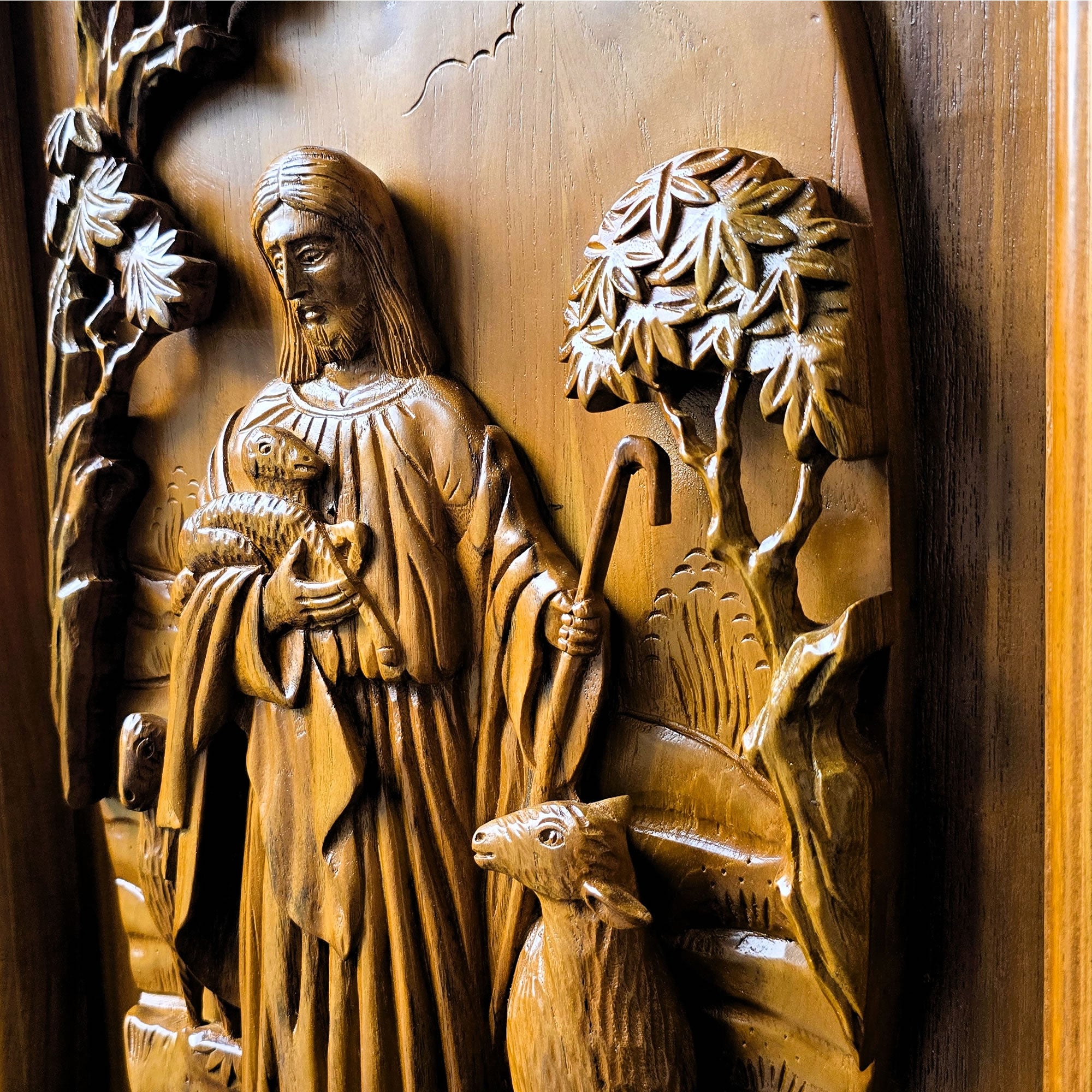Detailed closeup of solid teak wood carving showing dimensional relief details of Jesus Christ as the sacred shepherd, hand-crafted wall sculpture.