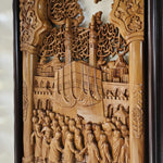 An ornate hand-carved wooden wall plaque depicting a historical or religious scene with a large ship, a crowd of figures, and intricate architectural details, framed in dark wood.