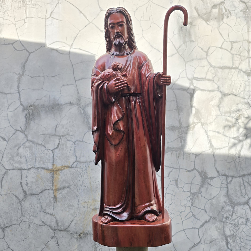 Statue of Jesus the shepherd holding a staff against a textured wall background