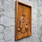 Wooden relief sculpture of a figure with a sheep on a gray textured wall.