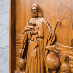 Wooden relief of a shepherd with a lamb on a textured wall.