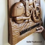 A hand is holding a carved wooden wall plaque featuring a motorcycle and the words 'HARLEY-DAVIDSON' in raised lettering. The plaque is made of solid teakwood and is shown against a plain indoor wall.