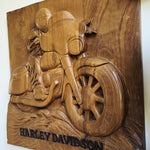 A hand-carved wooden wall plaque featuring a detailed relief of a Harley-Davidson motorcycle and rider, with the text 'HARLEY DAVIDSON' carved at the bottom, shown against a plain light background.