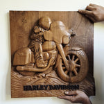A rectangular wooden wall plaque featuring a carved relief of a Harley-Davidson motorcycle and rider, held up by hands against a plain light wall.