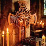 A carved wooden religious wall cross featuring a face with a crown of thorns and the inscription INRI, displayed against a stone wall with lit candles and an old book in a warm indoor setting.