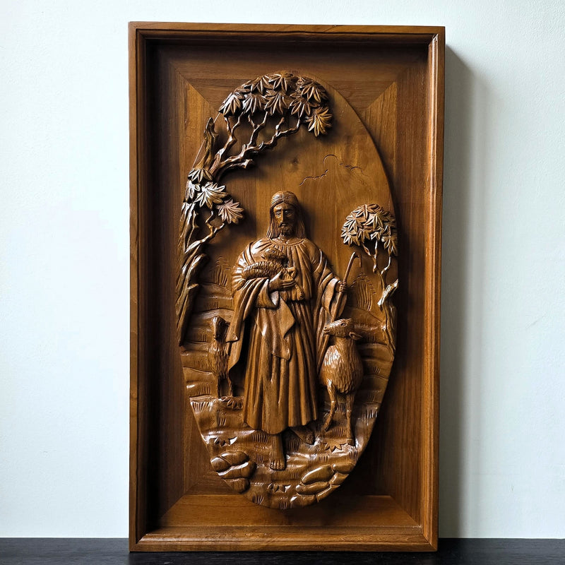 Hand-carved teakwood relief panel depicting Jesus the Good Shepherd holding a lamb under a tree canopy, 40 by 50 cm religious wall art.