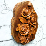 Side view of hand-carved teakwood roses sculpture highlighting the 3D relief carving and the thickness of the solid wood on a gallery wall